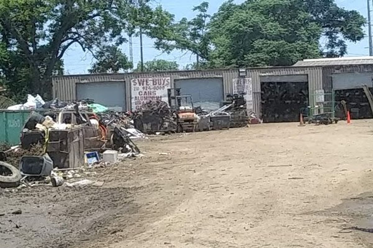 Primary Auto Recycling and Towing Service: Dirt lot with scrap piles in front of a metal building with roll-up doors and a hand-painted sign