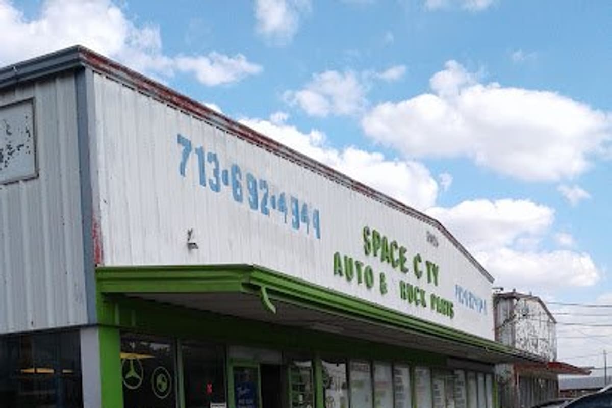 Space City Imports: Single-story auto parts shop with a green awning, painted sign and phone number, and green bollards along the front