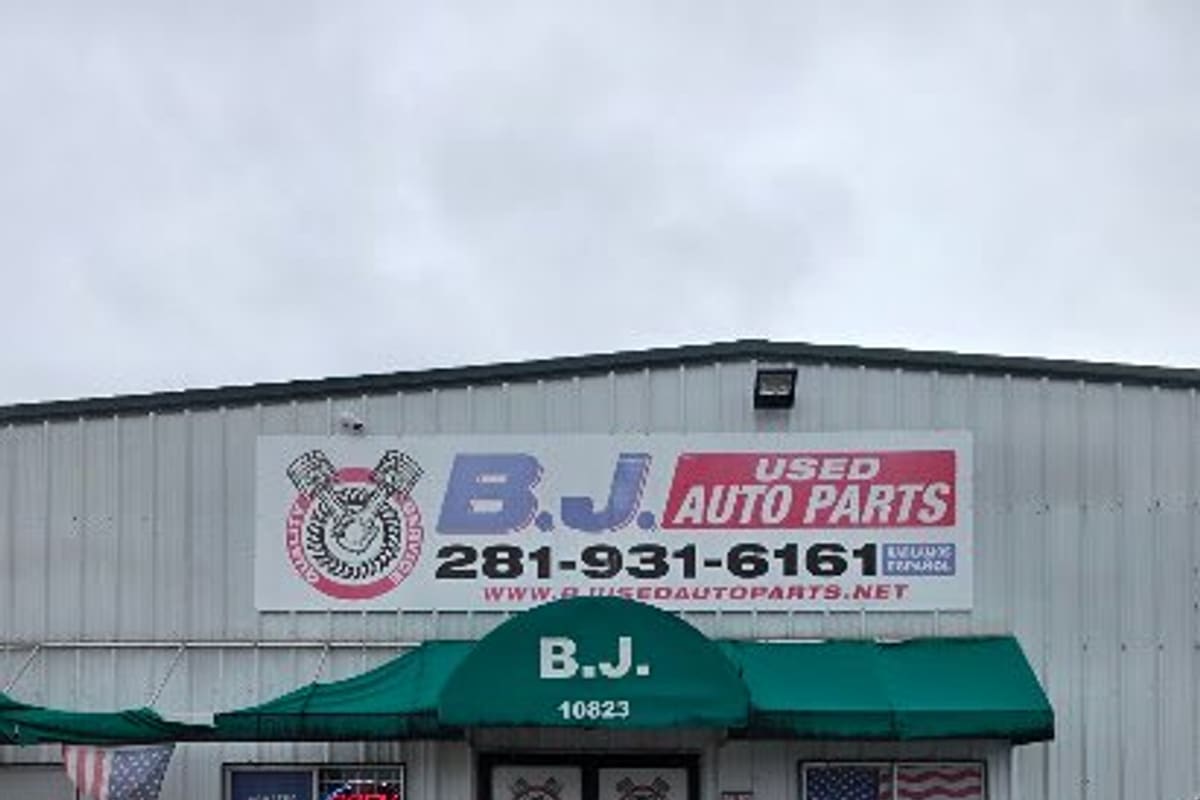 B.J. Used Auto Parts: Metal storefront with a large parts sign, green awning over glass double doors, and a striped parking area in front