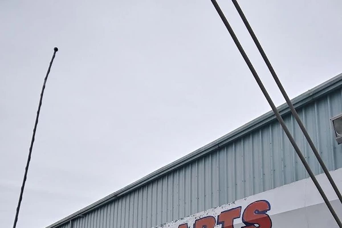 Deluxe Auto Parts: Metal warehouse building with a large painted auto parts sign over the entrance, a tree and lawn in front