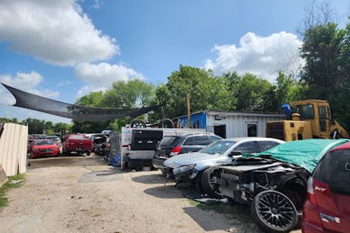 Unity Auto Parts & Service: Gravel salvage yard with wrecked cars parked in rows, a yellow loader, and a small metal building under a blue sky