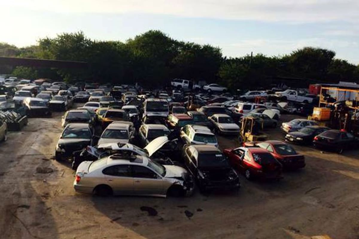 Affordable Auto Salvage: Wide view of a salvage yard packed with rows of wrecked cars on a dirt lot with trees behind