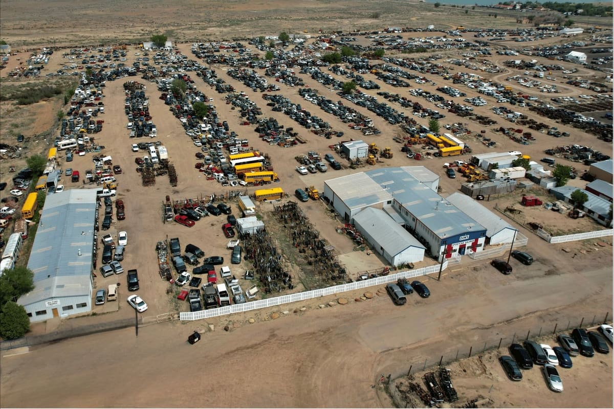 Dons Sportcar and Salvage Yard: Aerial view of a large salvage yard with rows of cars and school buses, metal-roofed buildings, and a parking area in front