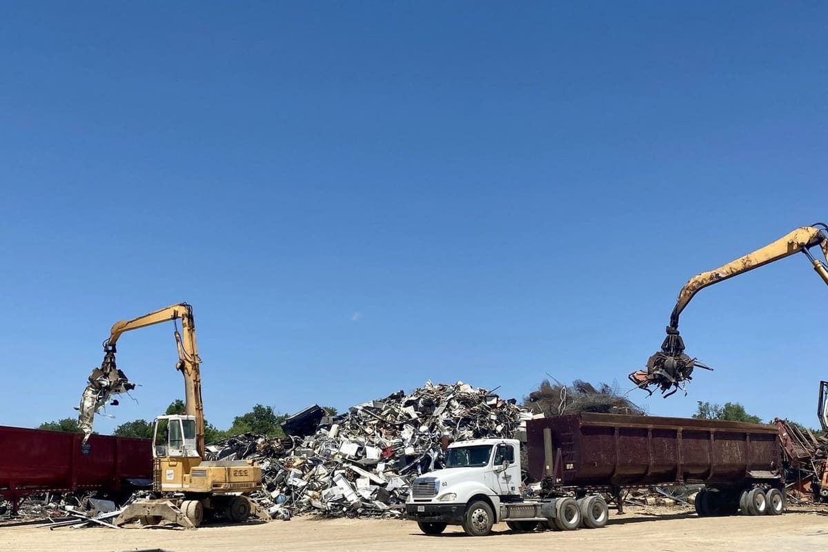 Stephenville Iron and Metal: Material handlers loading scrap metal into trailers beside a large scrap pile under a clear blue sky