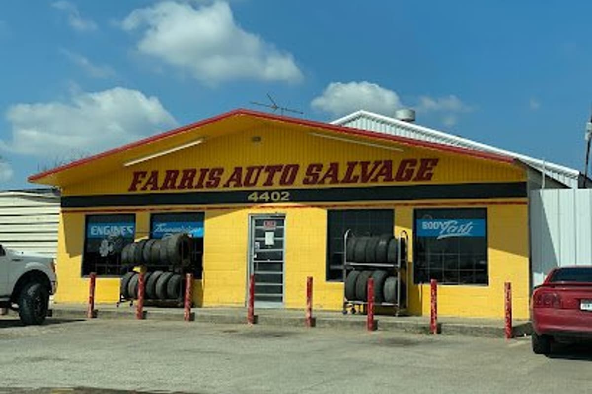 Farris Auto Salvage: Yellow single-story shop building with red trim, tire racks out front, and a painted sign above the door on a sunny day