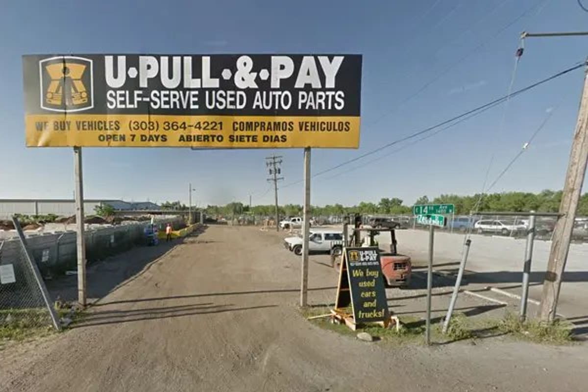 U-Pull-&-Pay Aurora: Gravel entrance road to a self-serve auto parts yard under a large yellow and black overhead sign