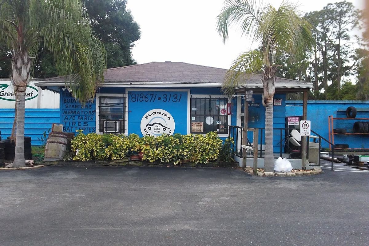 Florida Dial-a-Part: Blue single-story shop building with painted signage, palm trees, shrubs, and stacked tires in front of a paved lot