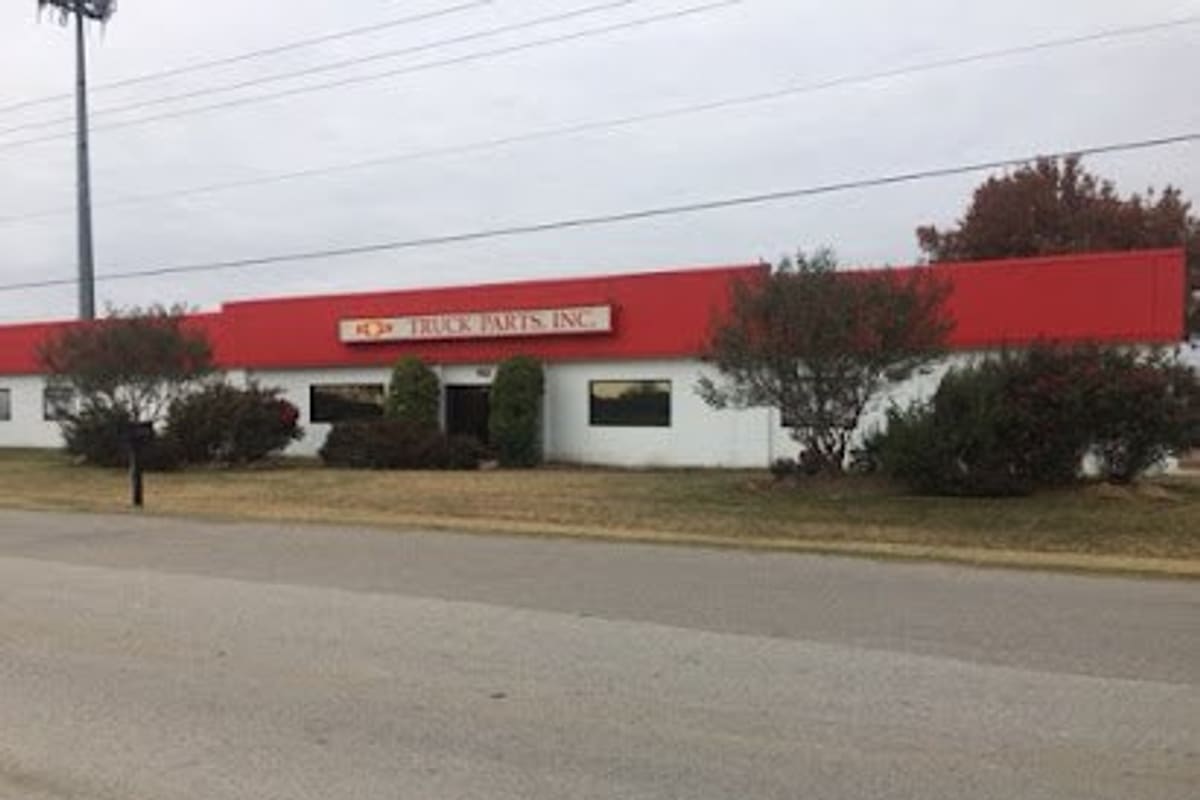 TNT Truck Parts: Single-story white commercial building with a red roofline and a Truck Parts, Inc. sign, seen from the road across a grassy lawn