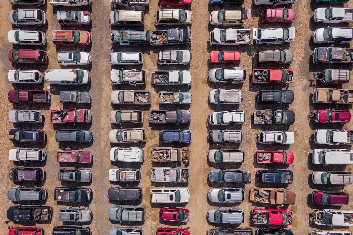 Byot BCS: Aerial view of a salvage yard with many cars and trucks parked in neat rows on dirt ground