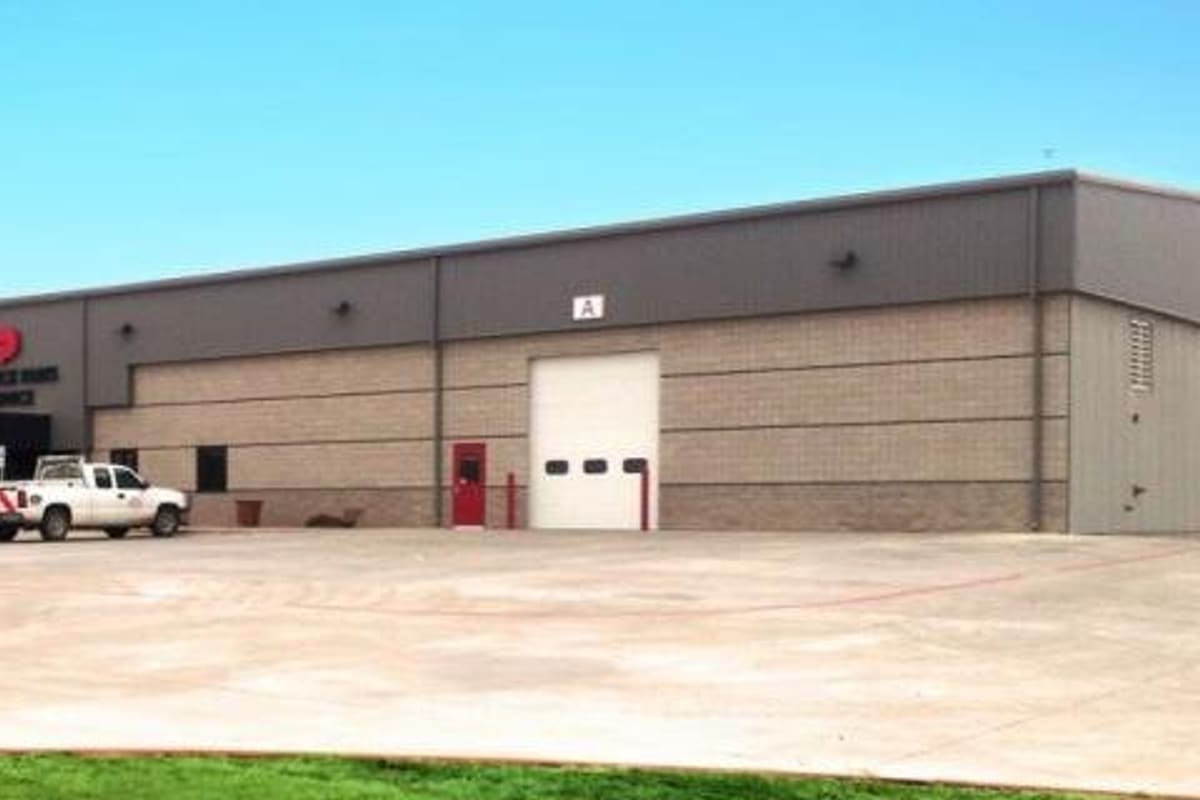 Inland Truck Parts & Service: Long single-story commercial building with tan brick and gray metal panels, roll-up bay doors, a pickup and semi truck parked on a wide concrete lot
