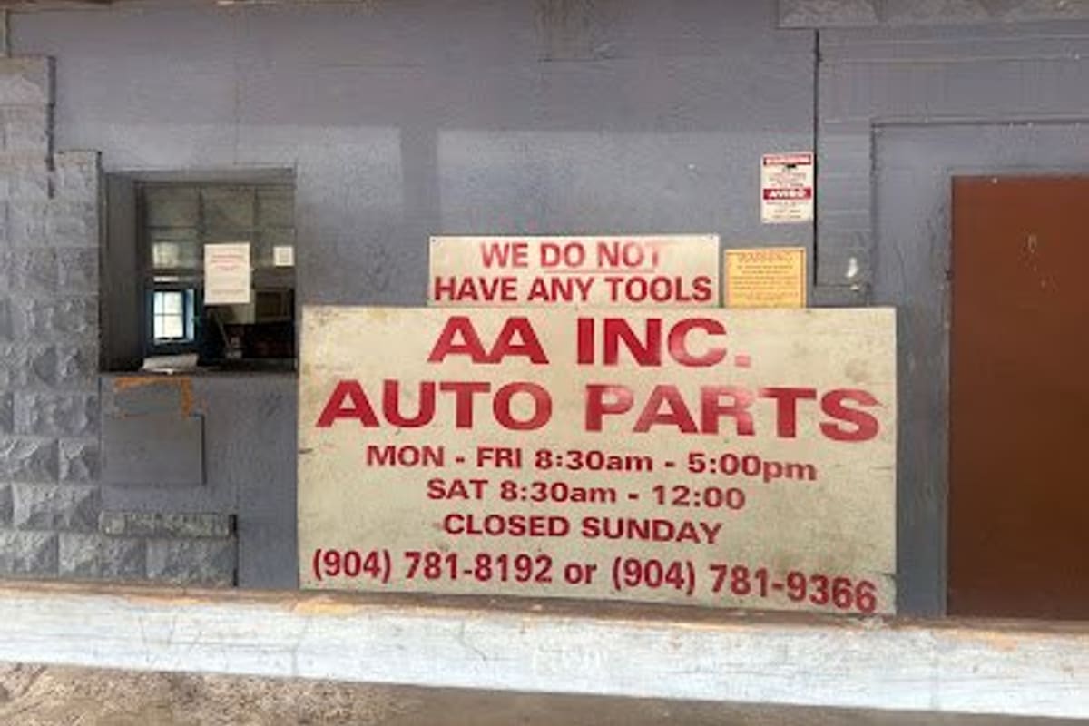 A a Auto Parts: Large red-lettered sign with business hours and phone numbers on a gray building wall beside a service window