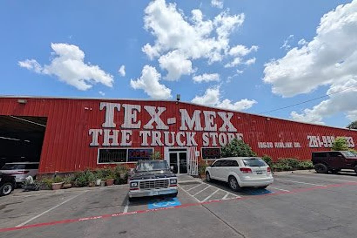 Tex Mex the Truck Store: Large red metal building with big white lettering, a glass entrance door, and parked vehicles in the front lot under a blue sky