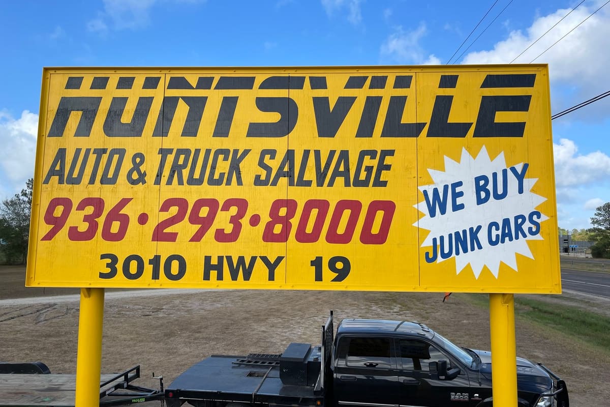 Huntsville Auto Parts: Large yellow roadside sign for an auto and truck salvage yard with phone number and a we buy junk cars burst