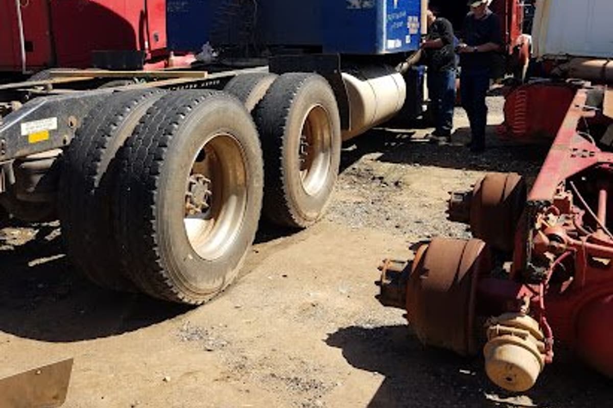 C & C Truck Parts: Dirt salvage yard with a blue semi truck cab and other truck cabs and axles parked on a sunny day