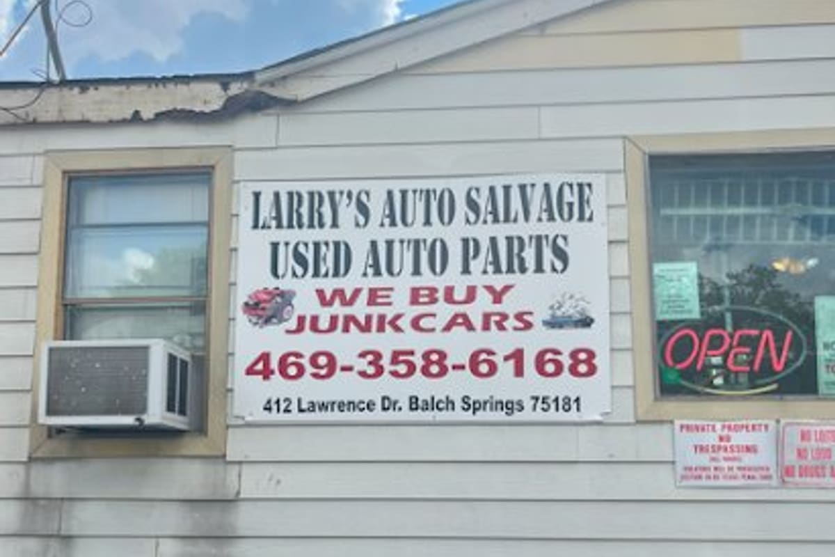 Larrys Auto Recycling: White sign reading auto salvage, used auto parts and we buy junk cars on the front of a cream-colored building with an open sign