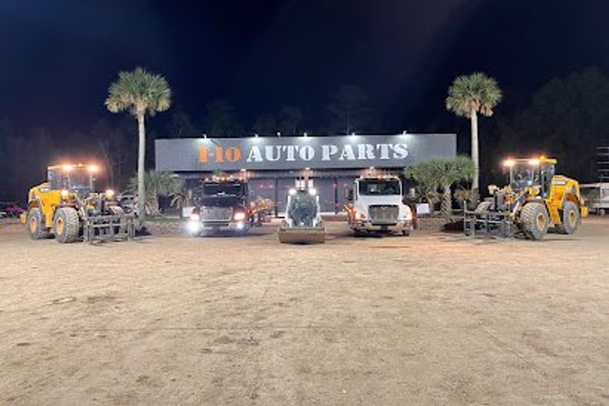 I-10 Auto Parts: Night view of a building with a large auto parts sign, trucks and yellow loaders parked in front on a dirt lot