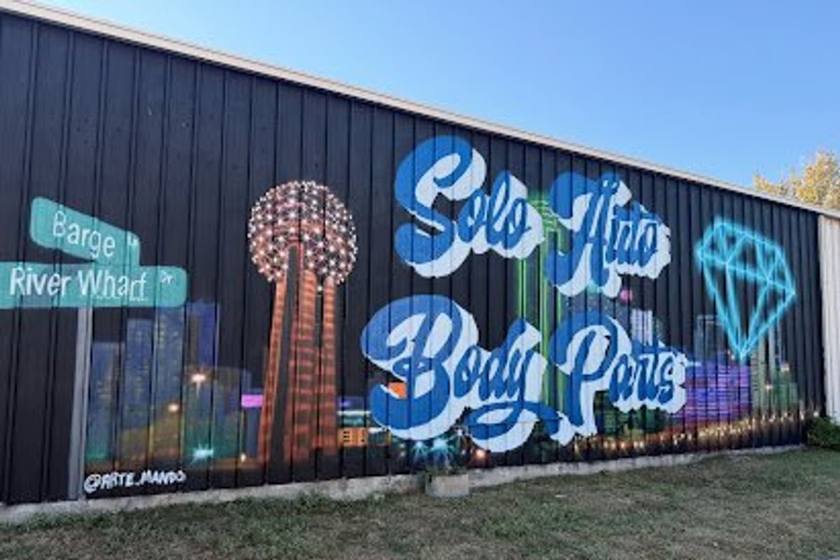 P&B Auto Body Parts: Black metal building wall with a colorful mural of the Dallas skyline, Reunion Tower and a lettered auto parts name, with grass in front