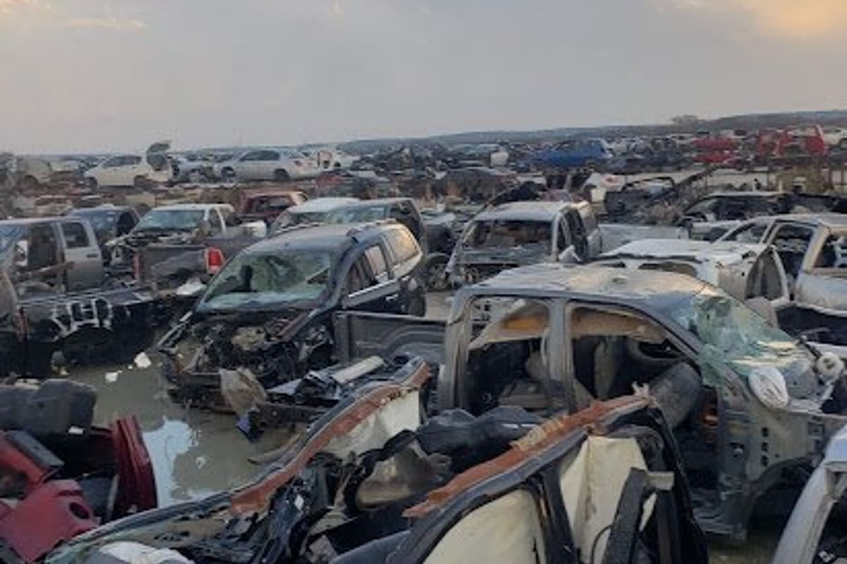 Completely Chrysler Used Auto Parts: Wide view of a salvage yard with rows of wrecked cars and trucks stretching toward the horizon under a cloudy sky