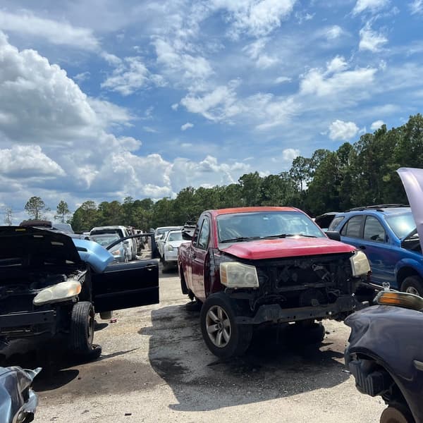 Pick Your Part - Daytona: Wrecked cars with open hoods parked on a gravel lot under a blue sky with trees in the background