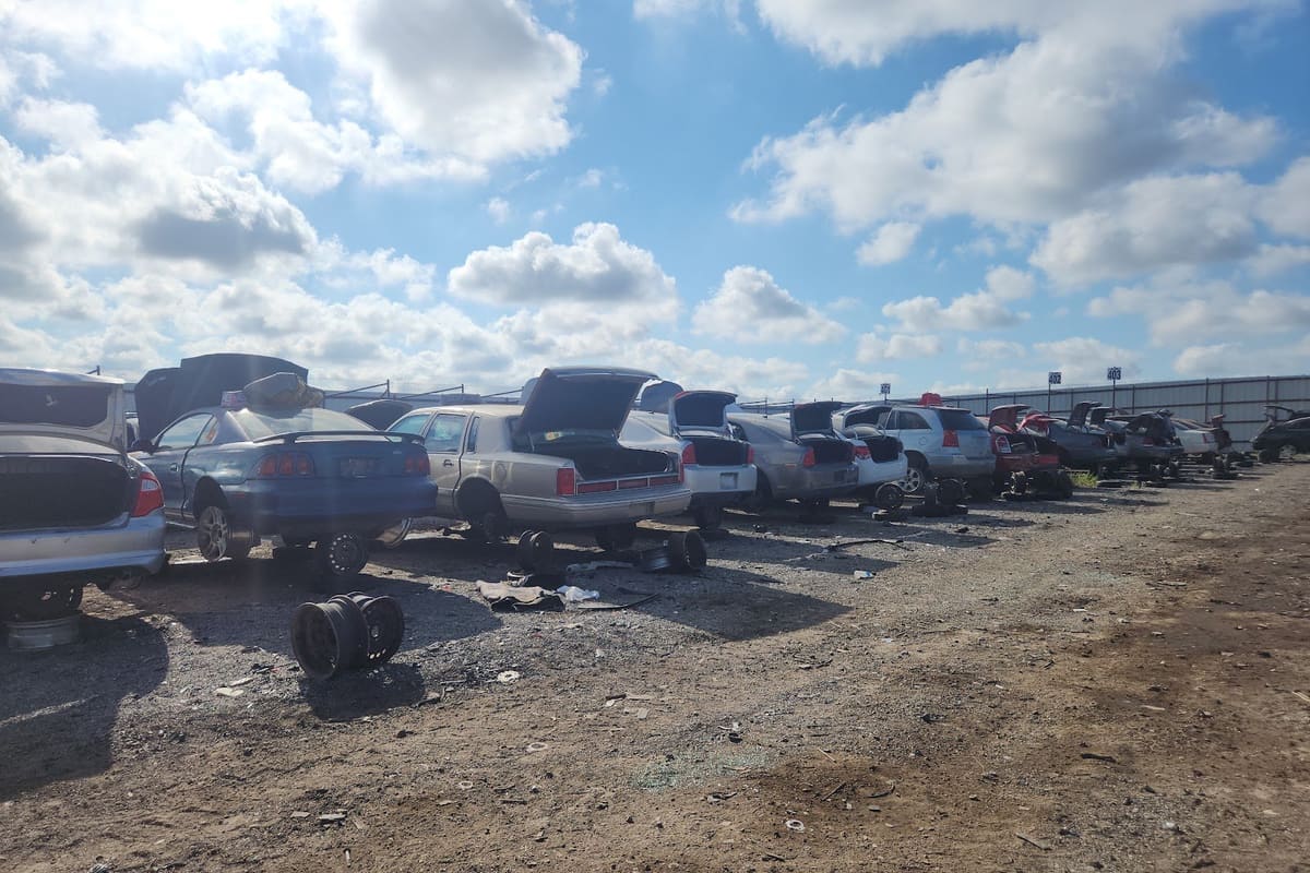 San Antonio Wrench A Part: Rows of wrecked cars with open trunks parked on a gravel lot under a blue sky with clouds