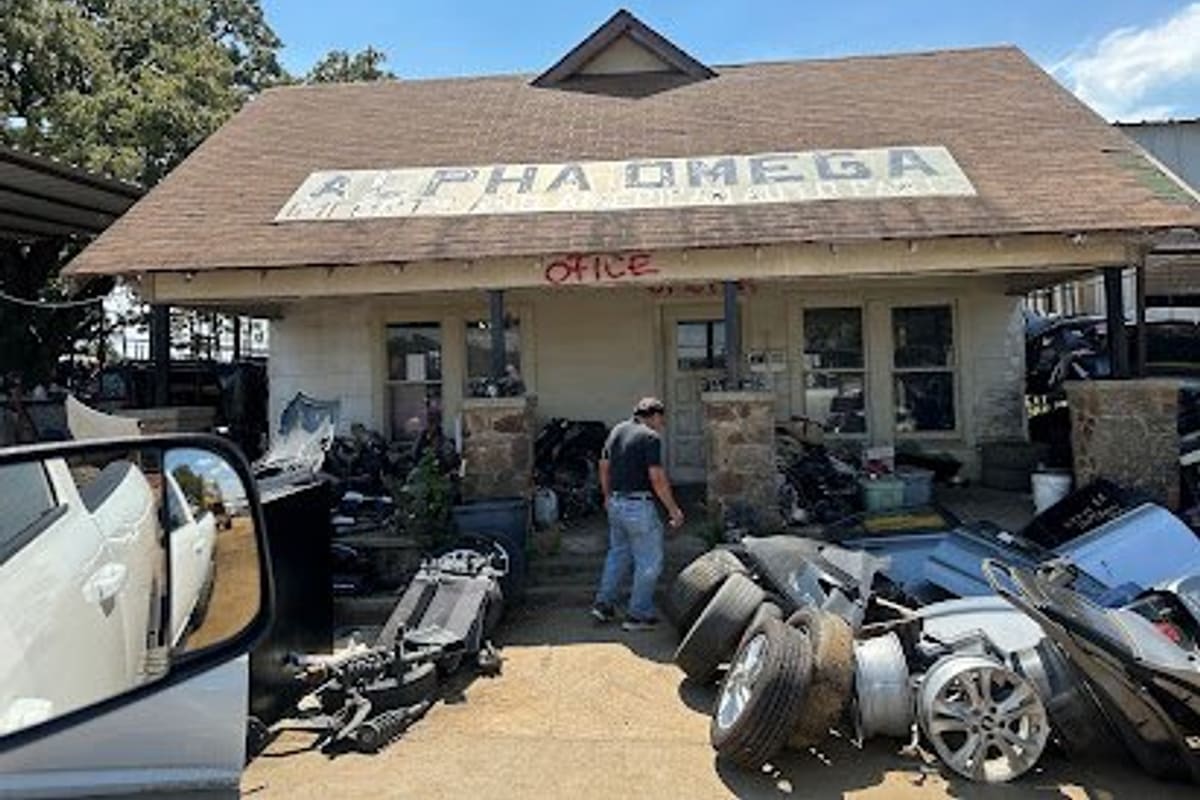 Alpha-Omega Imports: Single-story office building with a large painted rooftop sign and "Office" written above the porch, surrounded by tires and auto parts