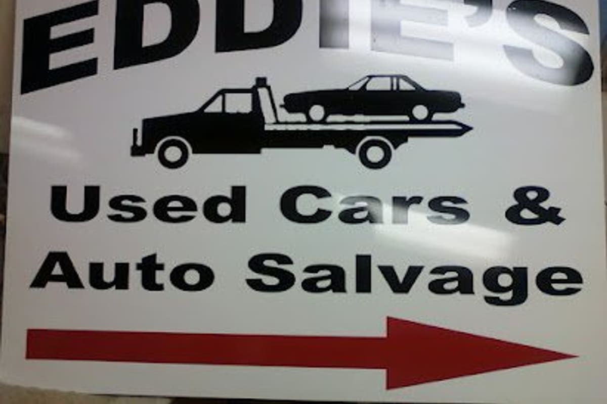 Eddie's Auto Salvage & Garage: White directional sign with a tow truck carrying a car, reading Used Cars & Auto Salvage, with a red arrow pointing right