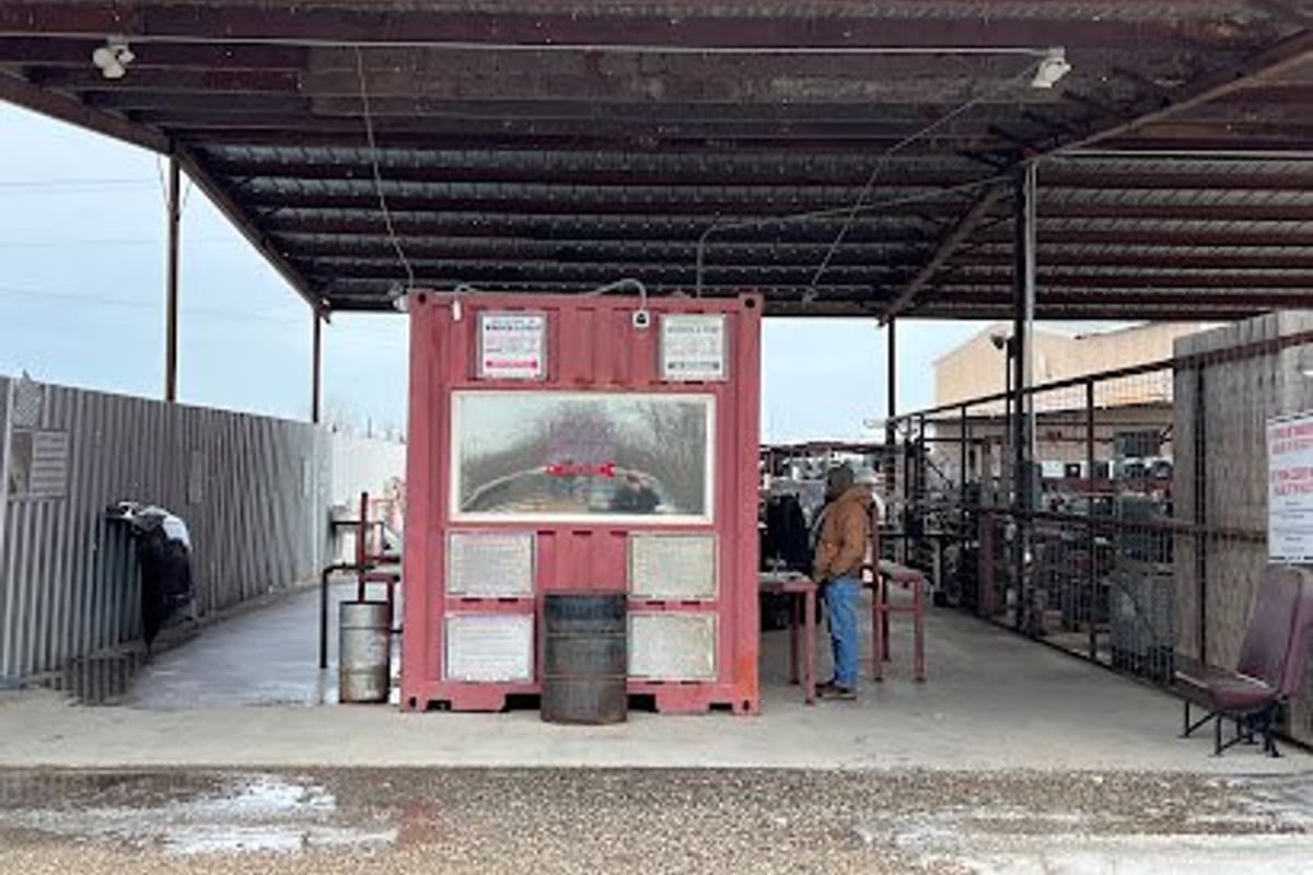 Late Model Wrench A Part: Covered entrance area with a red shipping container booth and posted notices under a metal roof at a salvage yard