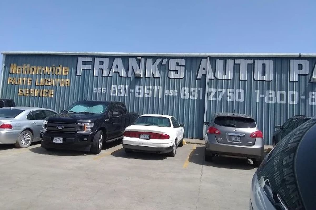 Frank's Auto Parts: Blue corrugated metal building with large painted lettering and phone numbers, cars parked in a paved lot in front