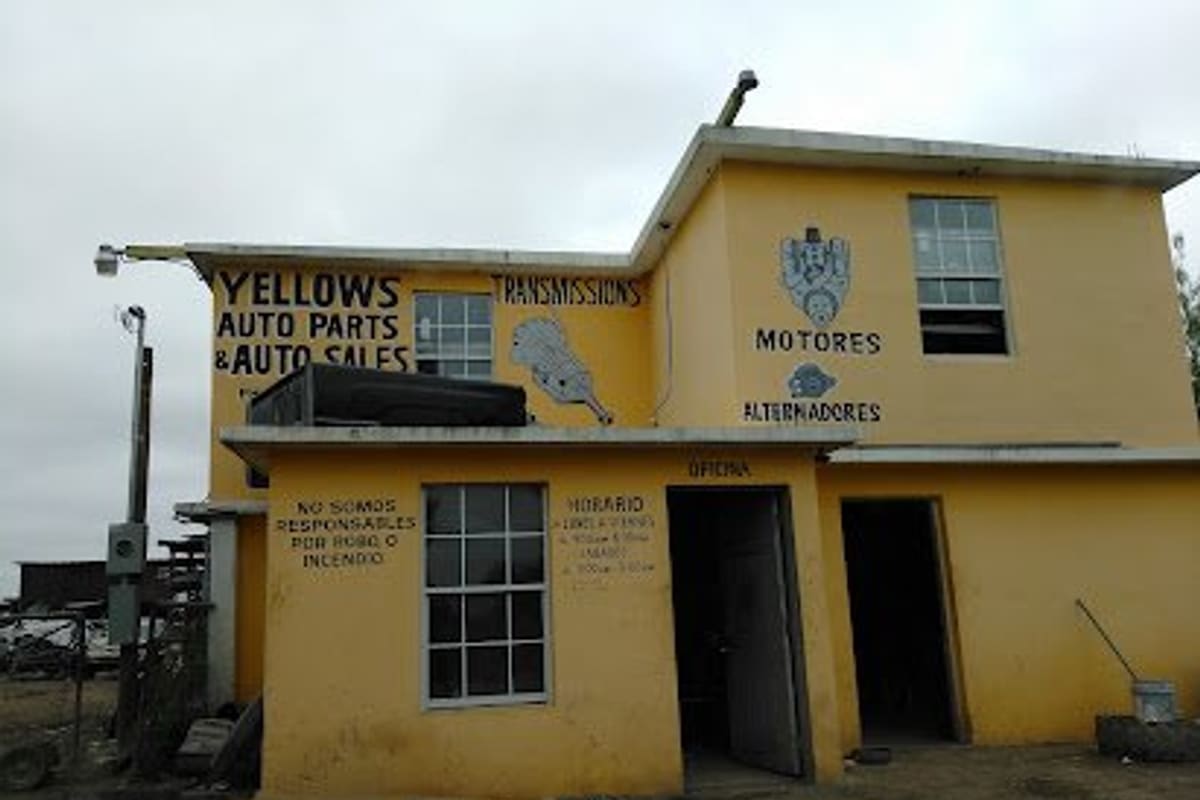 Yellow's Auto Sales and Auto Parts: Two-story yellow building with painted signs for auto parts, transmissions, motores and alternadores, and open doorways below