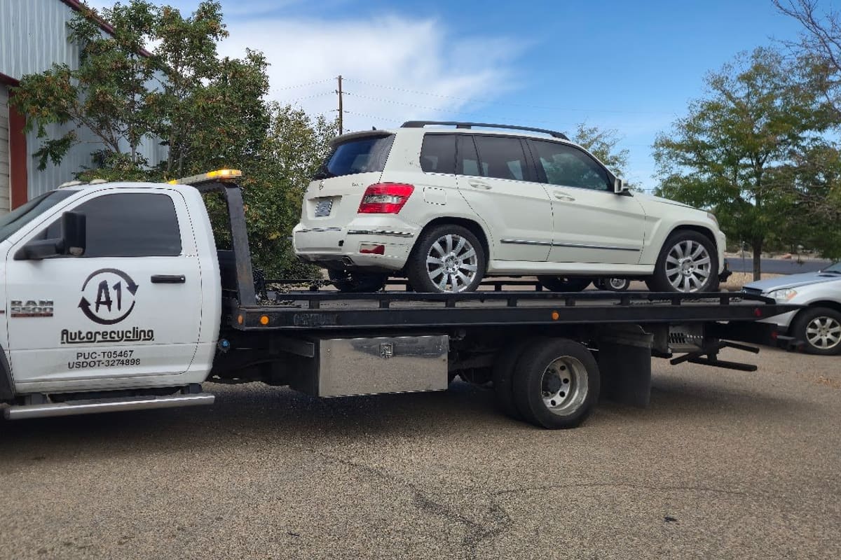 A and A Auto Recycling: White flatbed tow truck carrying a white SUV in front of a metal warehouse building with a roll-up door