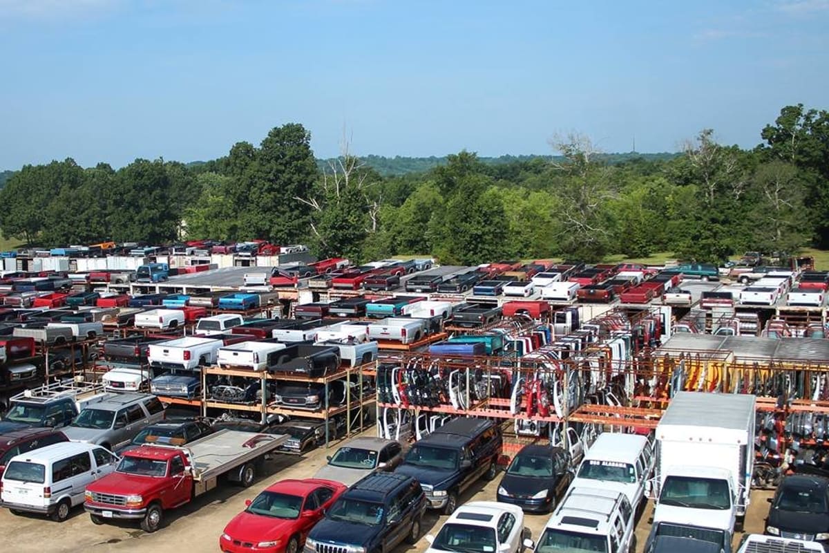 Bobby White Motor: Aerial view of a salvage yard with rows of truck beds, racks of doors, and parked cars and vans