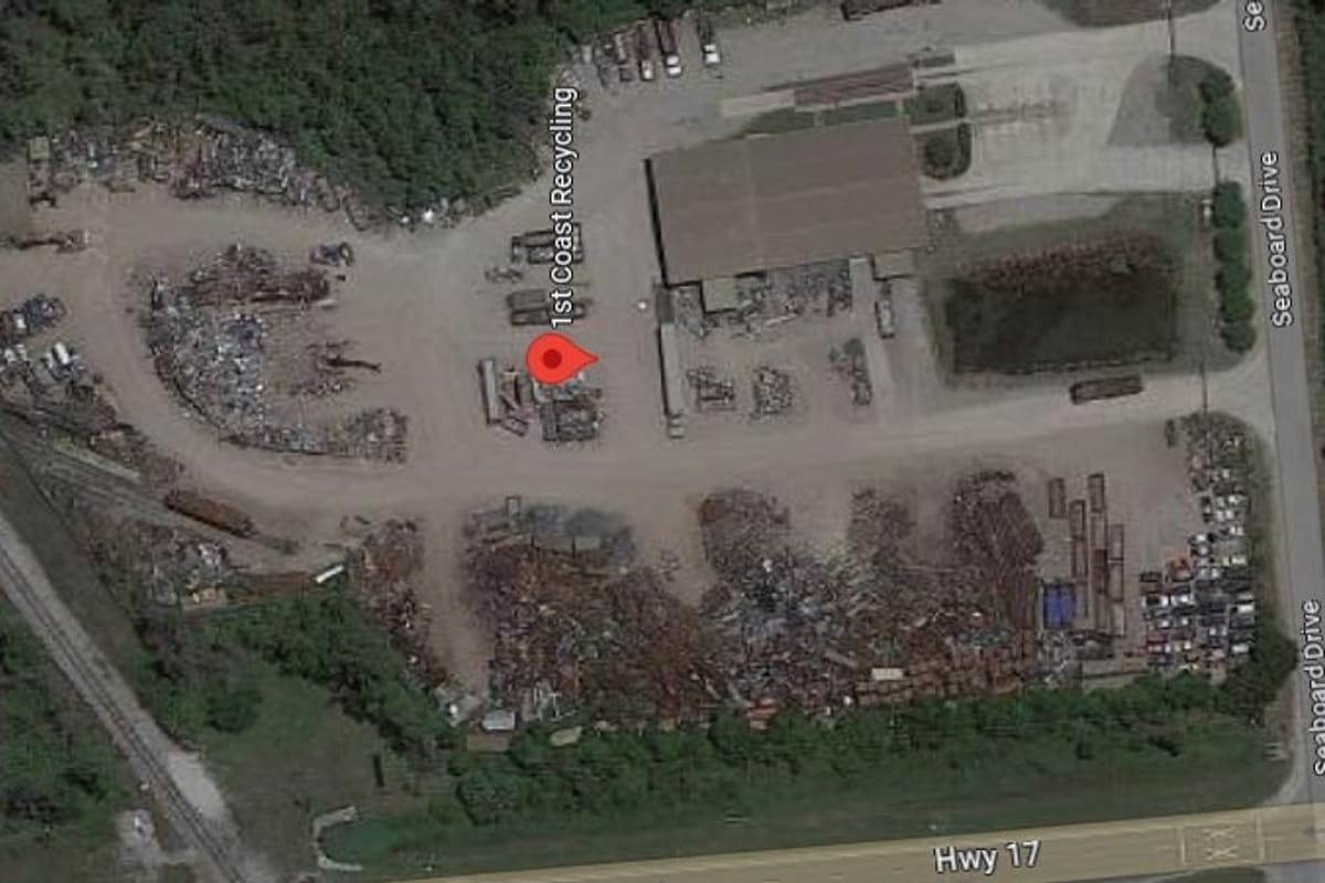 1st Coast Recycling: Aerial view of a salvage yard with scrap piles, vehicles and a large warehouse building beside a highway and railroad