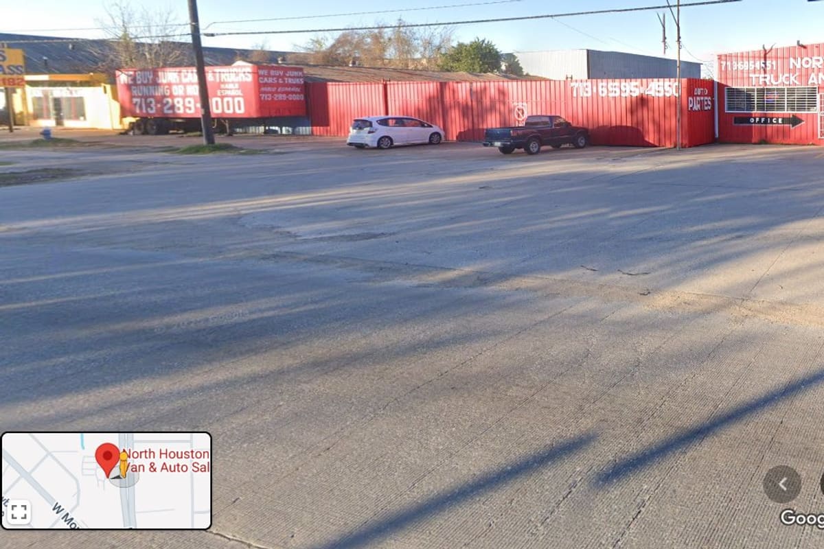 North Houston Truck and Auto Salvage: Red metal salvage yard building with office sign and painted phone numbers, seen from a wide concrete lot