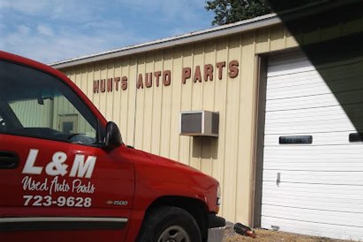 Hunt S Auto Parts: Tan metal shop building with red lettering reading Hunts Auto Parts, a white garage door, and a red pickup parked in front