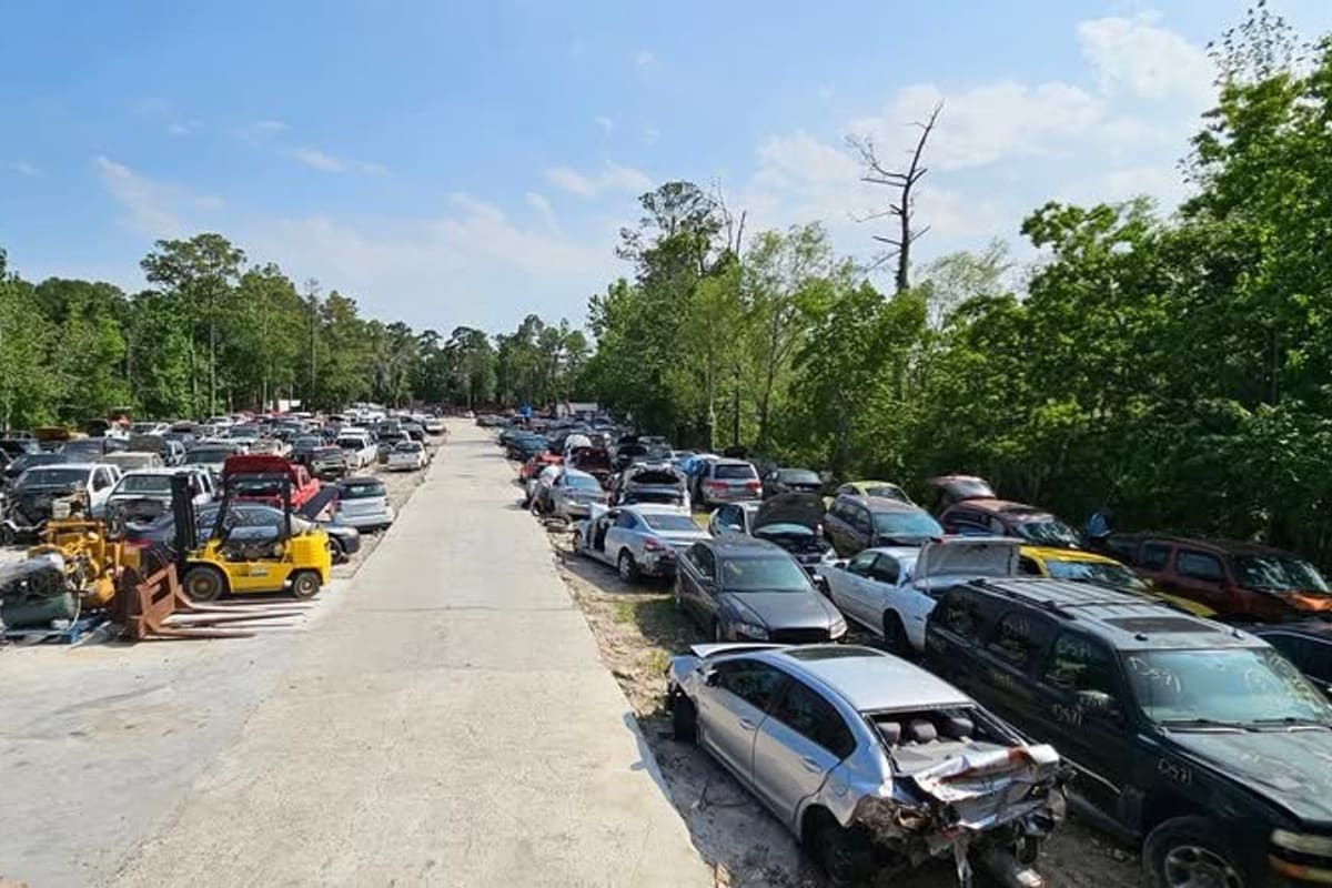 Duque Used Auto Parts & Sales: Wide view of a salvage yard with long rows of wrecked cars on both sides of a concrete lane and a yellow forklift