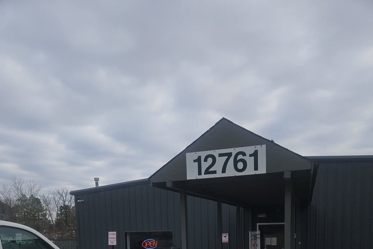 Auto Central: Dark metal building with a covered walkway entrance, house number 12761 on the gable, and an open sign in the window