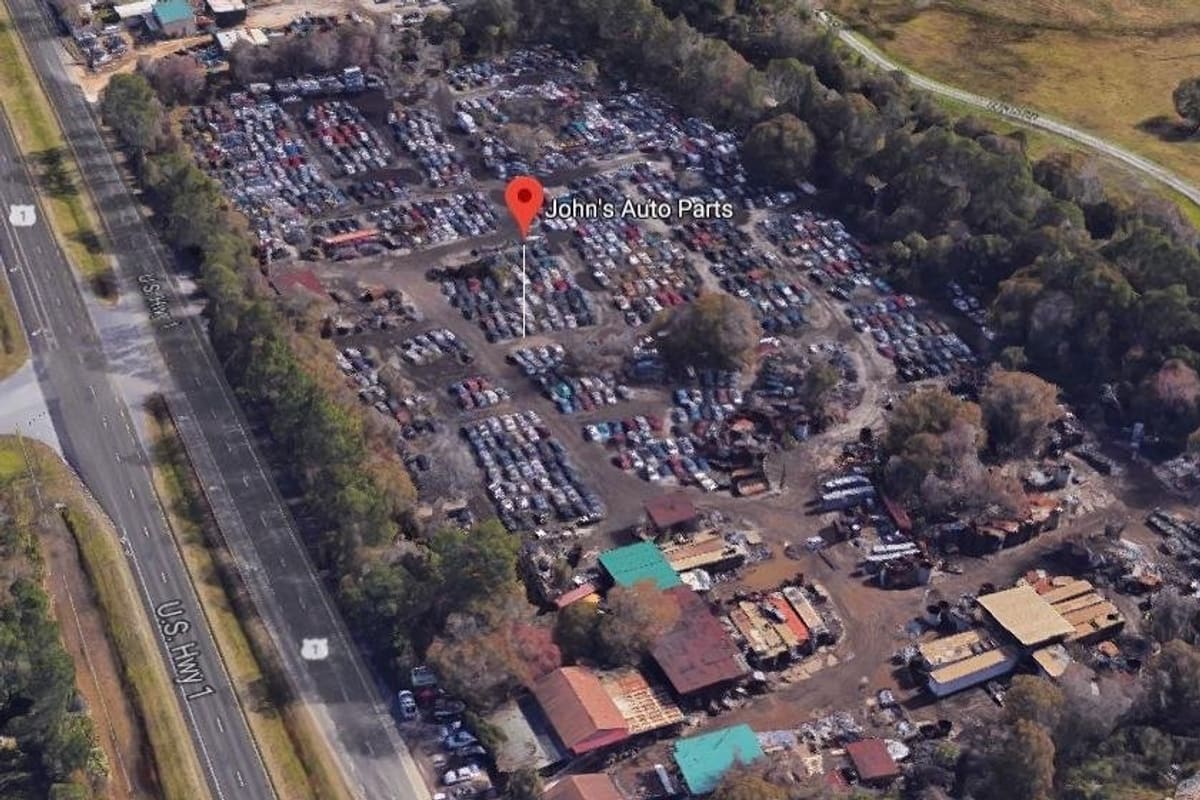 John's Auto Parts of Bunnell: Aerial view of a large salvage yard with rows of vehicles, several buildings, and trees beside a highway