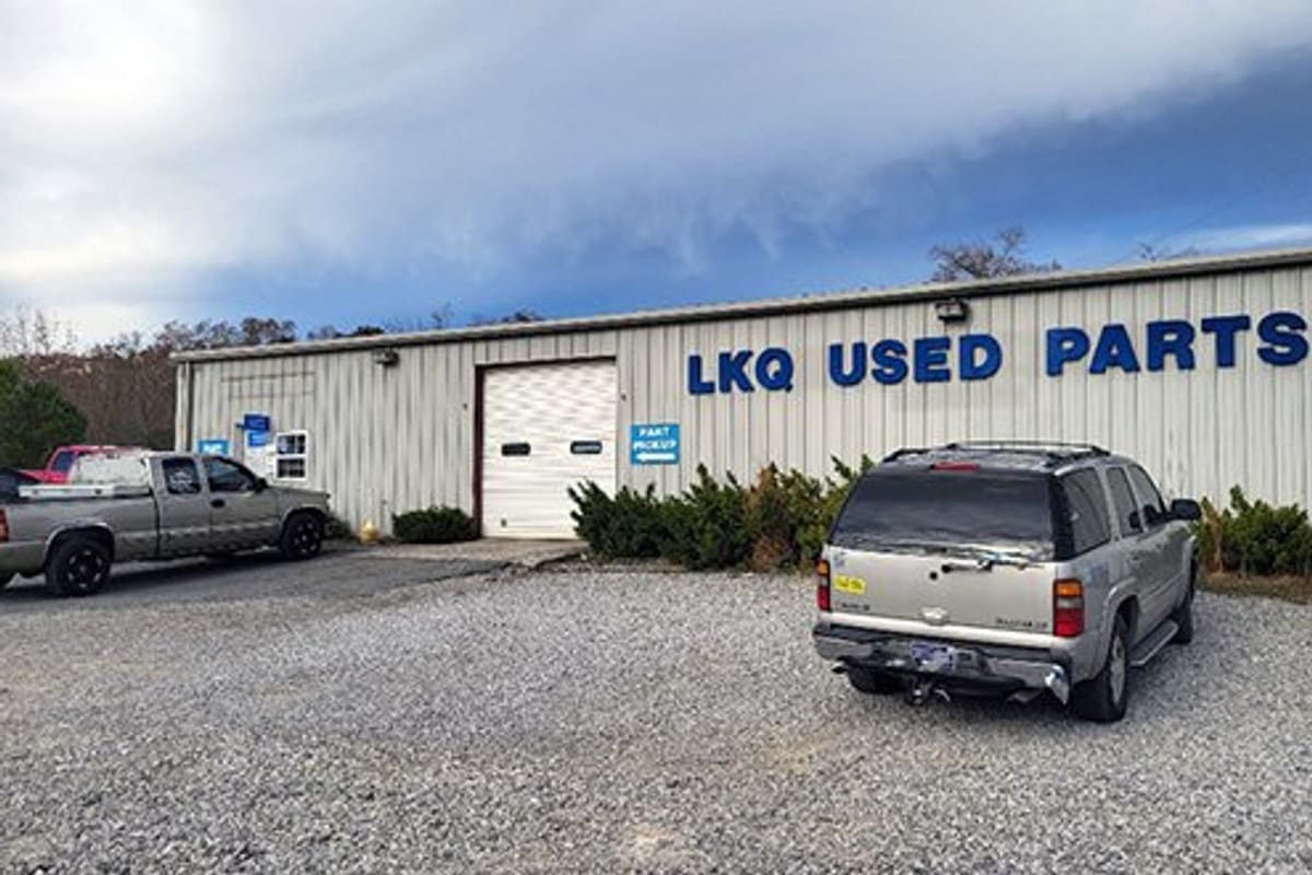 LKQ Manchester: Metal warehouse building with blue lettering, roll-up door, and vehicles parked on a gravel lot