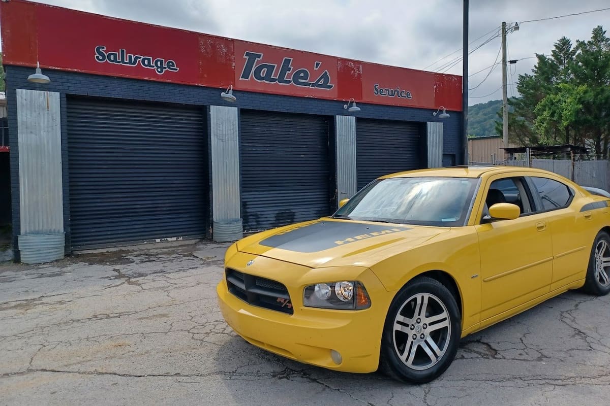Tate Service Center & Auto Salvage: Red-signed garage building with three roll-up doors and a yellow sports sedan parked in front on cracked pavement