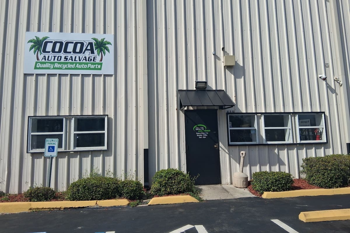 Cocoa Auto Salvage: Metal warehouse building with a company sign, shaded front door, shrubs and a parking lot in front