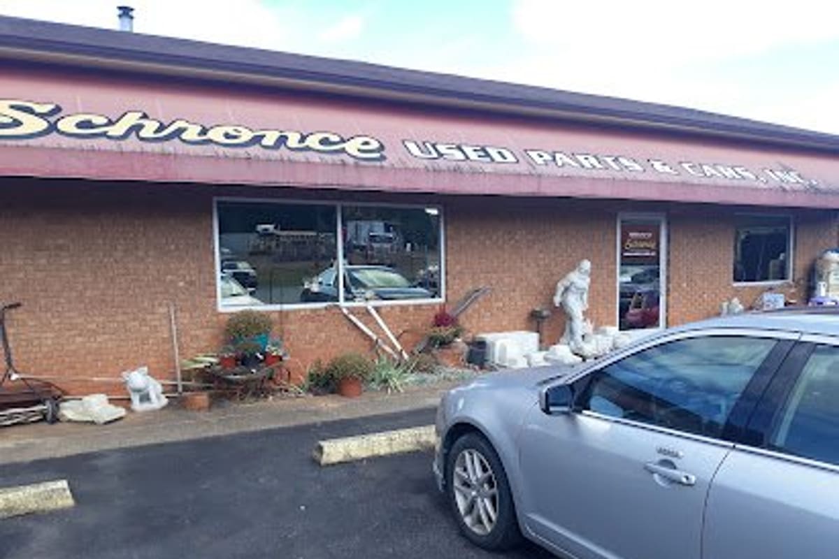 Schronce Used Parts and Cars: Brick storefront with a painted sign above the awning, garden statues by the wall and a silver car parked in front
