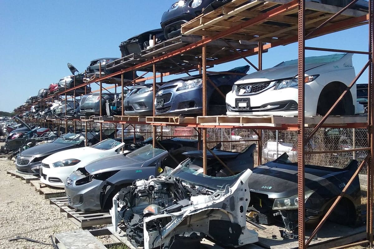 Grimes Truck & Auto Parts: Rows of salvage cars stacked on metal racks and pallets in an outdoor auto salvage yard under a clear blue sky