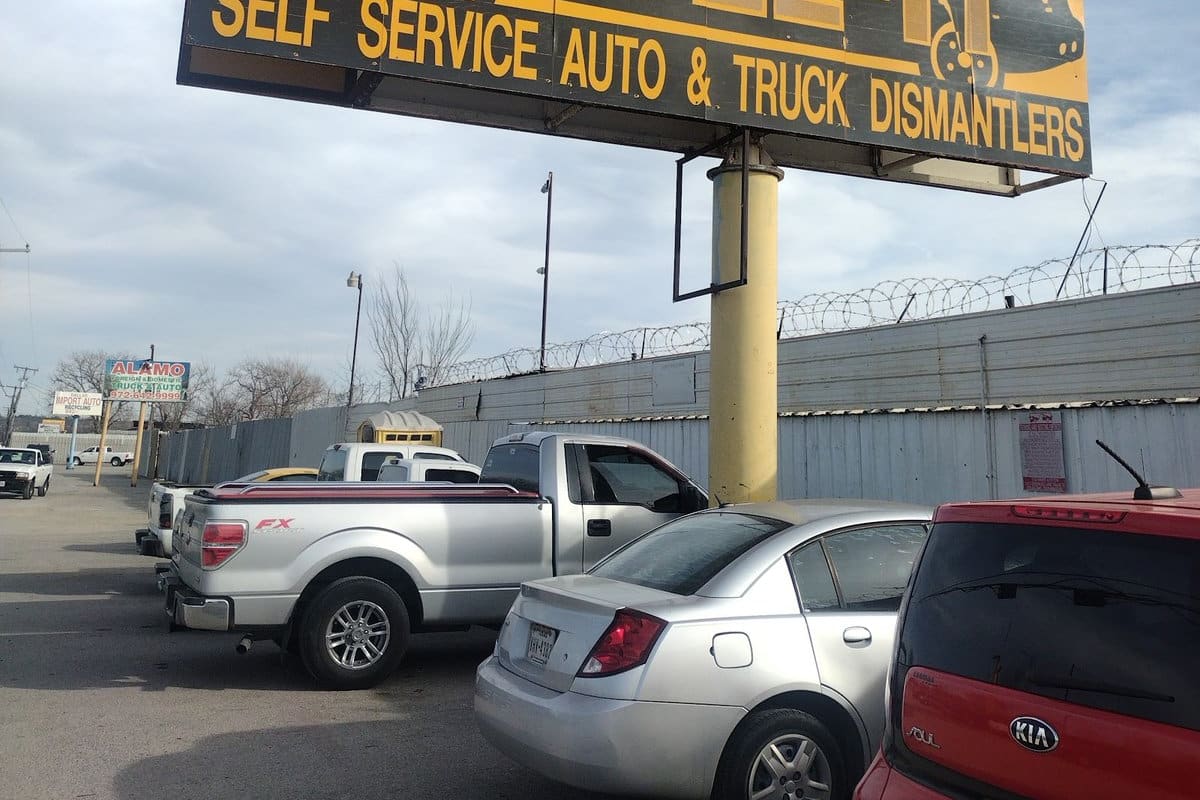 U Pull It Auto & Truck Salvage: Large yellow roadside sign reading U-Pull-It Self Service Auto & Truck Dismantlers above a parking lot with a fence
