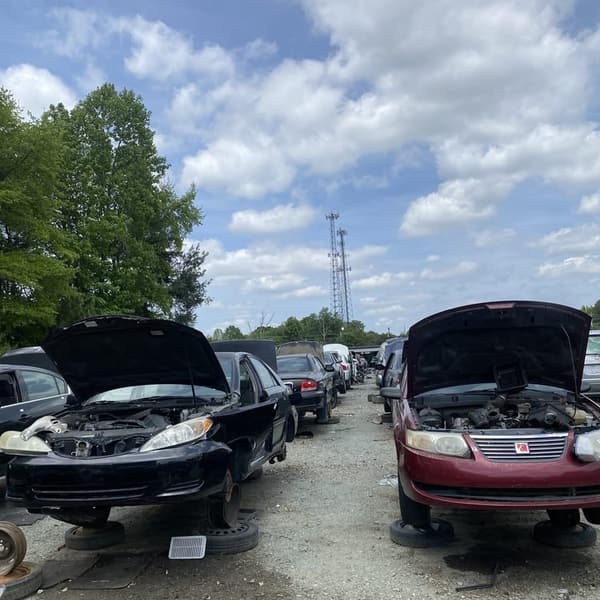 Pick Your Part - Greensboro: Rows of salvage cars with open hoods on gravel in a self-service junkyard under a partly cloudy sky