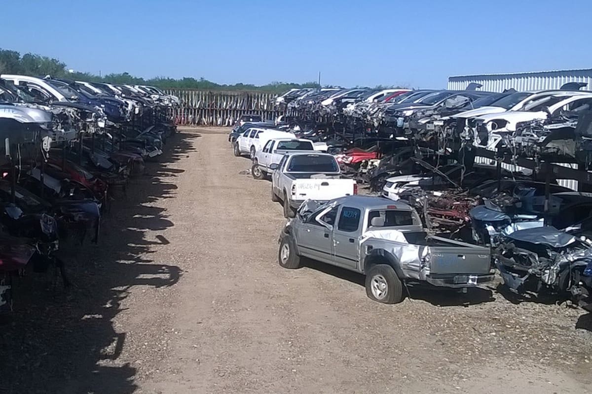 Pharr Auto Parts: Wide view of a dirt lane between tall racks of stacked salvage vehicles under a clear blue sky