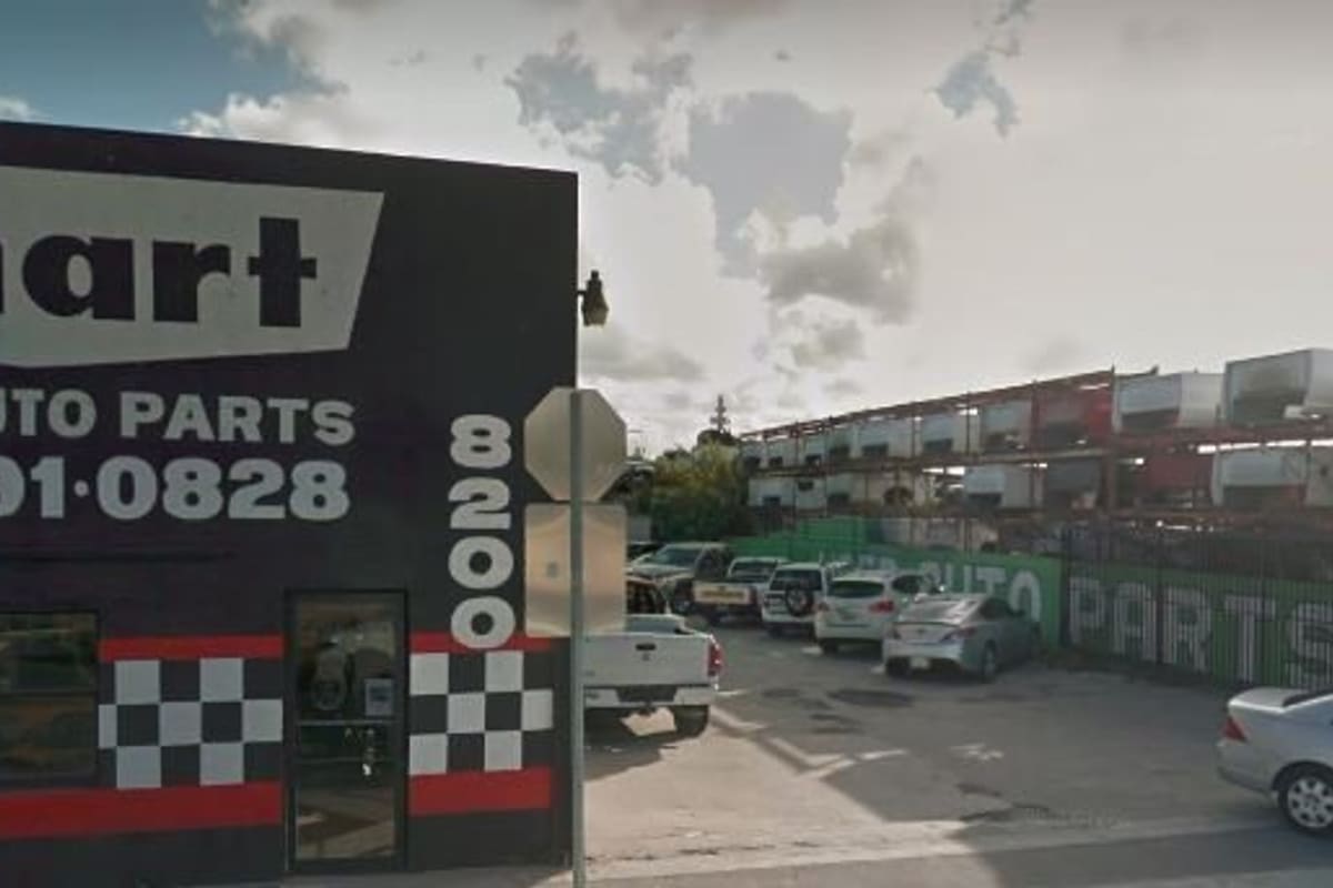 Smart Used Auto Parts: Black building with checkered stripe and painted used auto parts sign beside a lot with parked cars and stacked vehicles