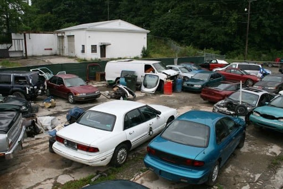 Worley's City Iron & Metal: Wide view of a salvage yard with rows of used and wrecked cars parked on a gravel lot beside a white building