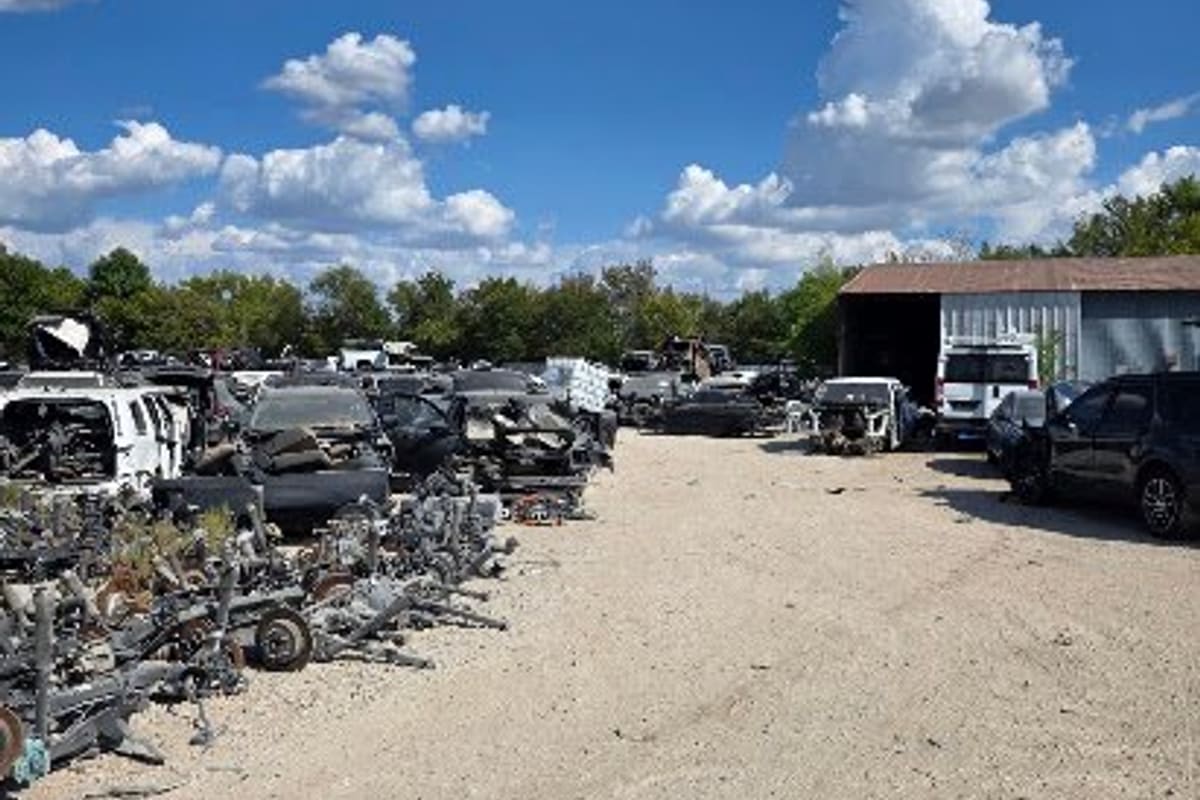 Kar Parts of Texas: Gravel salvage yard with rows of wrecked vehicles and auto parts, a metal shed on the right, under a blue sky