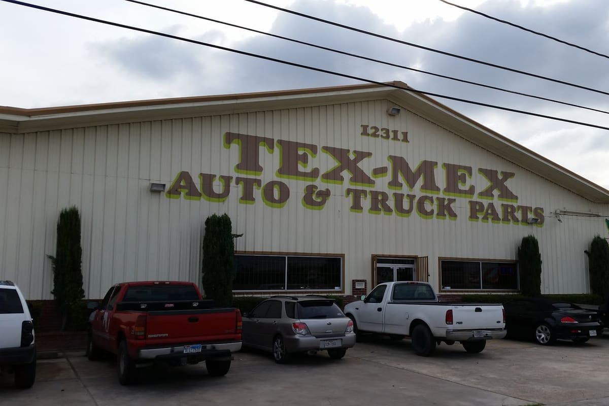 Tex-Mex Auto & Truck Parts: Large cream metal building with painted lettering reading Tex-Mex Auto & Truck Parts and trucks and cars parked in front