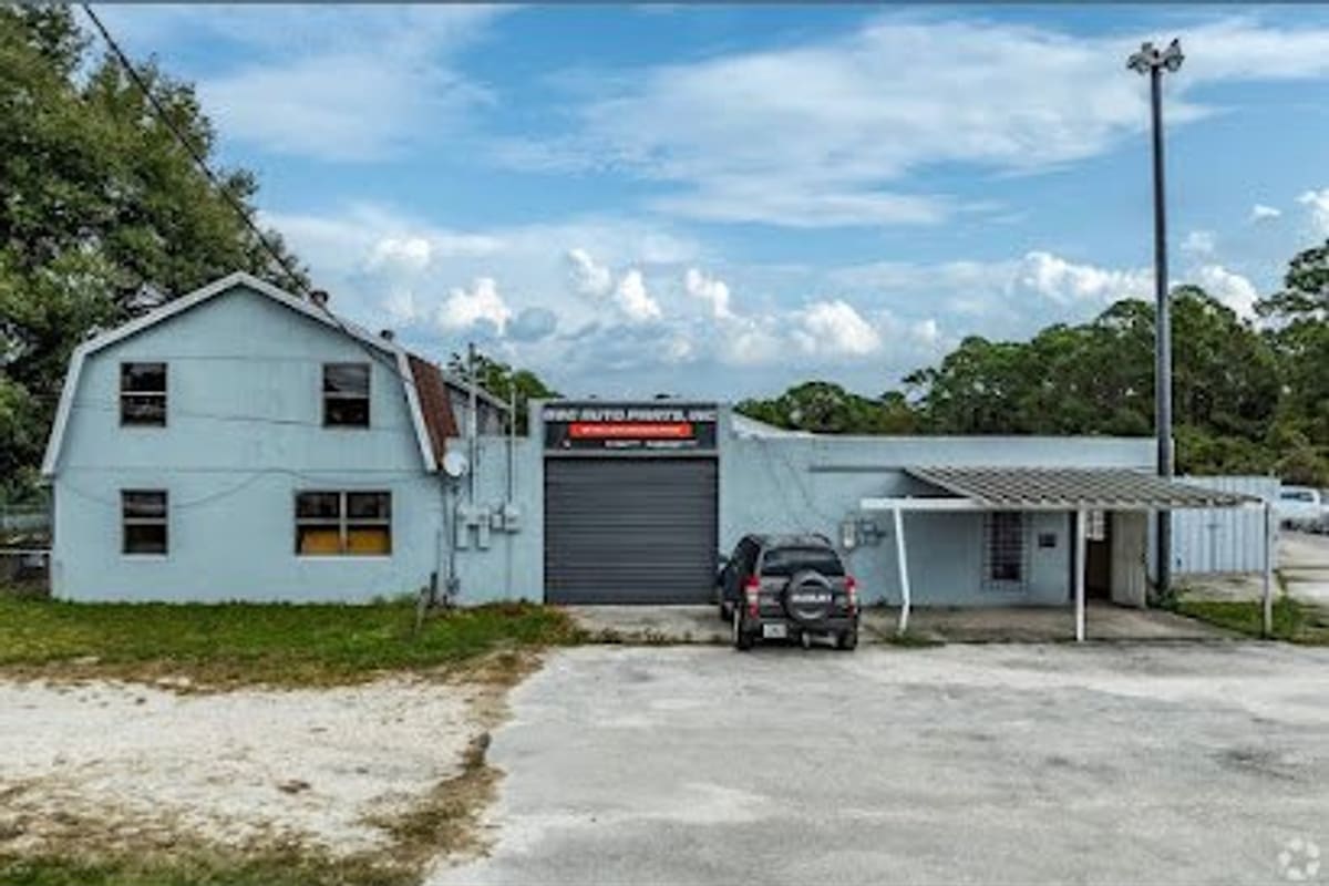 G & C Auto Parts: Light blue two-story building with a closed roll-up garage door, a covered side canopy, and a paved lot in front